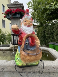 Gartenzwerg XXL mit Korb und Lampe als Gartendeko am Brunnen.