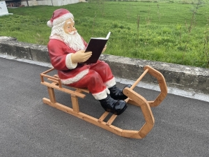 Weihnachtsmann auf Holzschlitten mit Buch schraeg fotografiert.