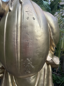Rueckendetail des grossen lachenden Buddha mit rotem Beutel