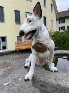 Sitzender Bullterier als Gartenfigur auf einem Brunnenrand.
