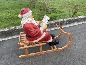 Weihnachtsmann mit Buch auf Schlitten in Rueckansicht.