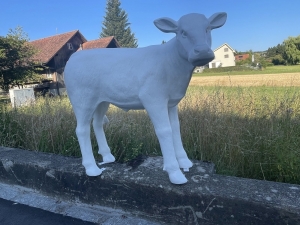 Weisse Kuhfigur lebensgross schraeg von vorne fotografiert.